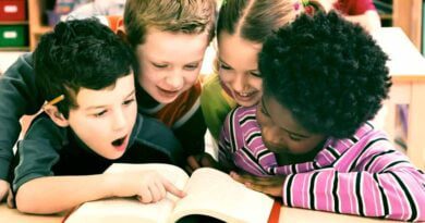 2 meninos e uma menina brancos e uma negra felizes lendo um livro juntos