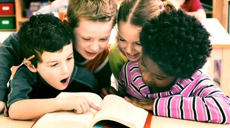 2 meninos e uma menina brancos e uma negra felizes lendo um livro juntos