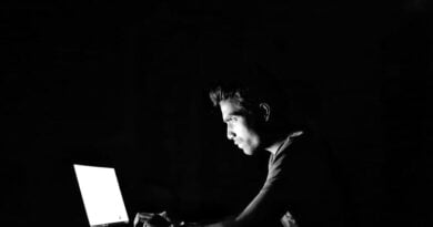Rapaz em frente a tela de um computador em sala escura