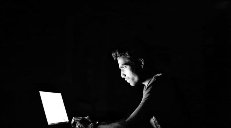 Rapaz em frente a tela de um computador em sala escura
